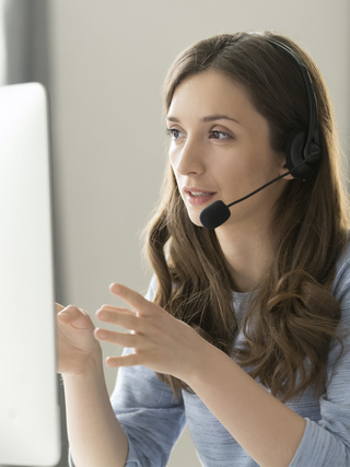 Serious call center operator in wireless headset talking with customer, woman in headphones with microphone consulting client on phone in customer support service, looking at computer screen close up