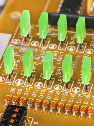Green rectangular light-emitting diodes in rows on a beige printed circuit board. Electronic components. Plastic LED lights, switch, resistor or microchip. Flexible membrane PCB of dismantled keybord.